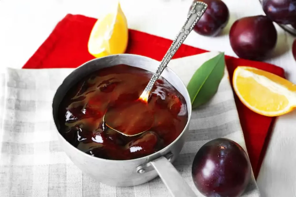 Tasty homemade plum jam in stew pot on wooden table closeup