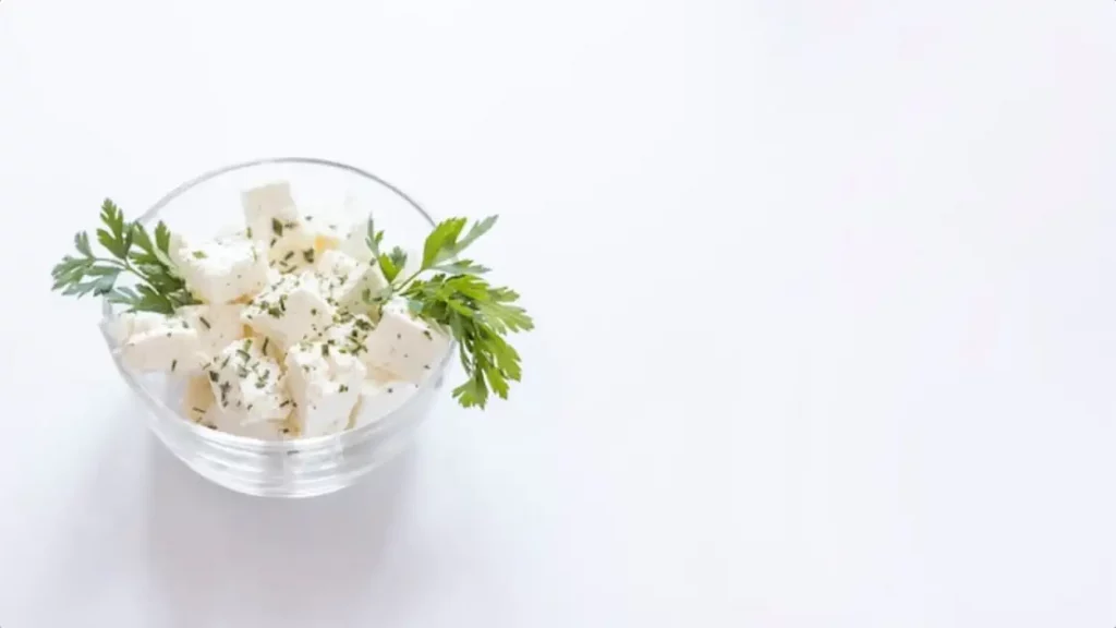 White cheese cubes with parsley in the glass bowl on white backdrop